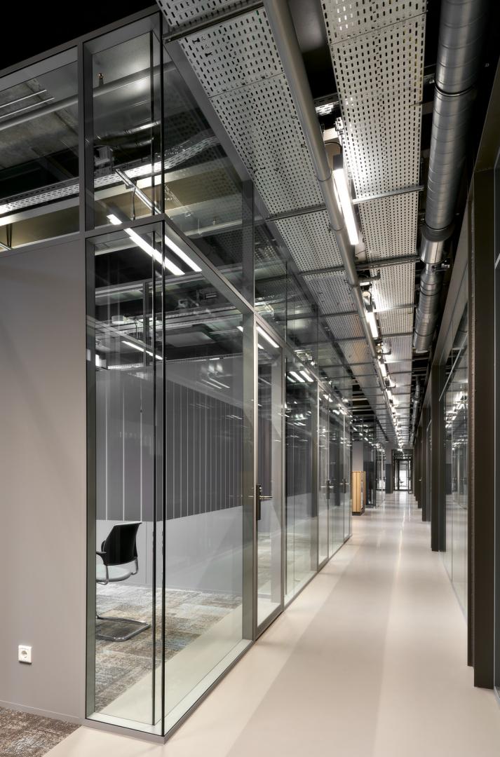 A corridor with a meeting room on the left side with glass partition 