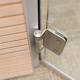 Detail of a stainless steel hinge of a DK42 door frame and a tampered glass door